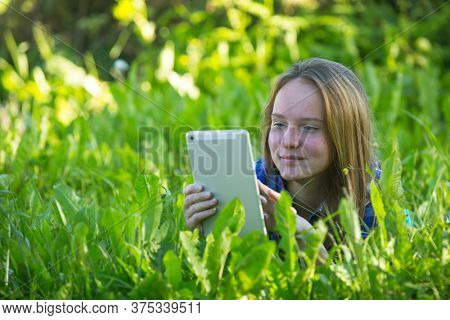 Teengirl with a tablet lying in the grass on the park.