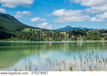 Weissensee Lake In Front Of The Mountains Of The Bavarian Alps Against A Blue Sky Near Fuessen, Allg