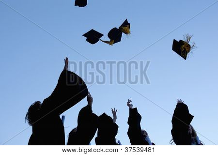 Angolo-colpo basso di cinque diplomati gettando loro cappelli nel cielo