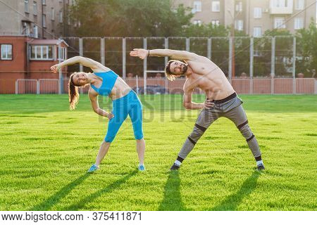 Attractive Young Couple Man And Woman 25 Years Old Are Doing Exercises On A Sunny Summer Morning On