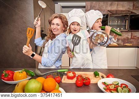 Funny children and their mother cook dinner together, they cut a salad of fresh vegetables. Happy family. Healthy eating.