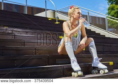 A stunner smiling summer closeup portrait of sexy young happy woman posing in a vintage roller skates, T-shirt, shorts posing on a road in city  hot summer day. Holidays and vacations.