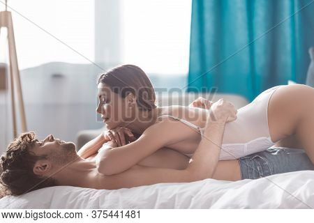 Side View Of Handsome Shirtless Man Embracing Sexy Woman In Bodysuit On Bed