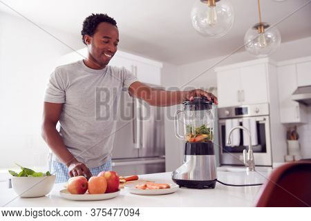 Man Wearing Pyjamas Standing In Kitchen Putting Fresh  Fruit And Vegetables Into Blender