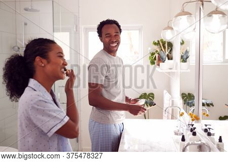 Couple Wearing Pyjamas Standing In Bathroom At Sink Brushing Teeth In The Morning