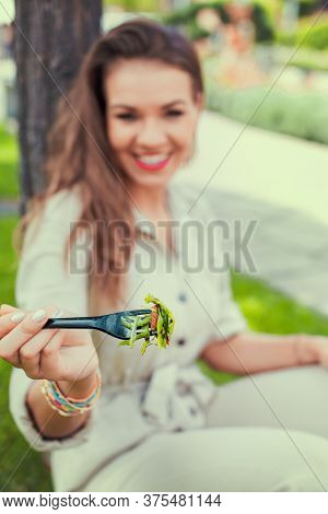 Happy Young Latina Woman Holding Salad With Toothy Smile In Park, Depth Of Field