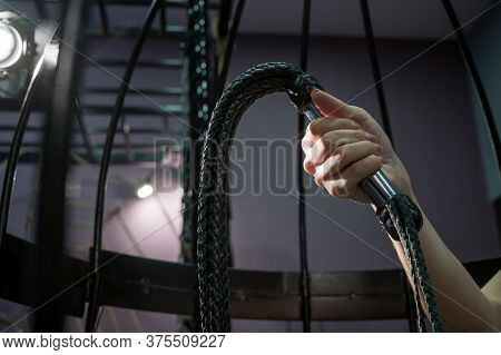 Female Hand With A Long Woven Leather Lash In A Cage. Bdsm Punishment And Pleasure. Cropped.