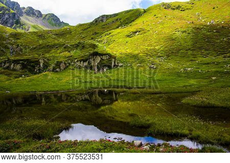 Small Alpine Lake Between The Green Fields And The Gray Granite Rock Of The Lagorai In The Trentino 