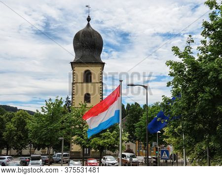 St. Michaels Or Old Tower In Market Square And Luxembourg National Flag Waving In Wind. Mersch, Luxe