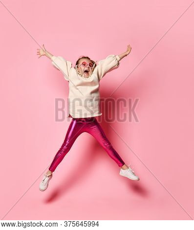 Cute Little Girl In Stylish Casual Attire Jumping Up Spreading Arms And Legs Widely And Shouting In 