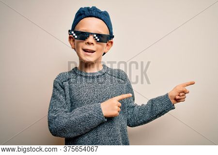 Young little caucasian kid wearing internet meme thug life glasses over isolated background smiling and looking at the camera pointing with two hands and fingers to the side.
