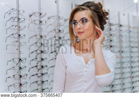 Happy Female Client Or Optician Is Standing With Set Of Glasses In Background In Optical Shop. Woman