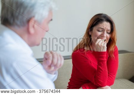 An Upset Woman Bites Her Nails At A Session With A Male Psychologist. Mature Gray-haired Psychothera