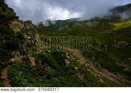 Path Climbs Between The Alpine And Granite Rocks Of Lagorai With Cloudy Skies Near Lake Levico In Tr