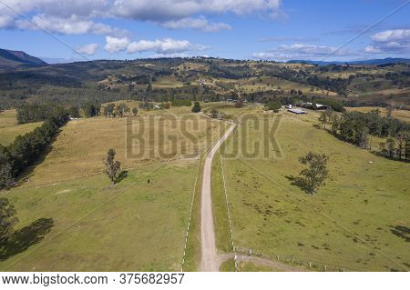 Aerial View Of A Dirt Road With White Fence Post Markers In A Green Agricultural Field