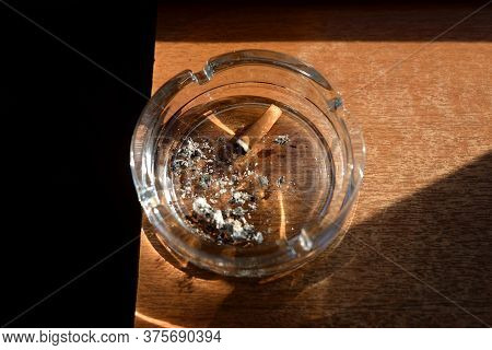 Ashtray With A Cigarette Butt On Wooden Surface.