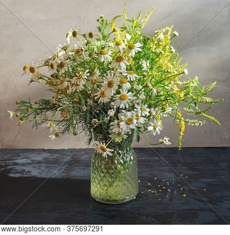 Light Bouquet Of Wildflowers With The Prevalence Of Daisies In A Glass Vase On A Dark Table