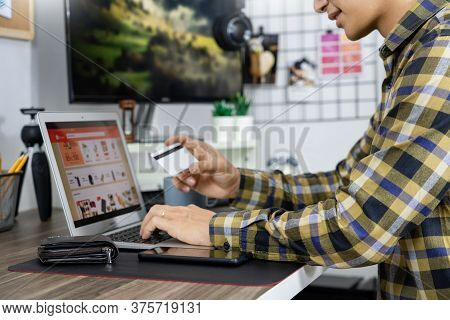 Asian Man Holding Credit Card To Online Shopping With Laptop Computer And Entering Security Code, In