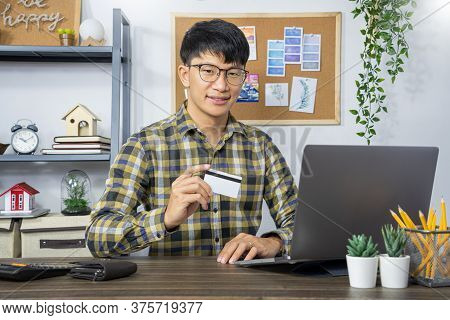Asian Man Holding Credit Card To Online Shopping With Laptop Computer And Entering Security Code, In