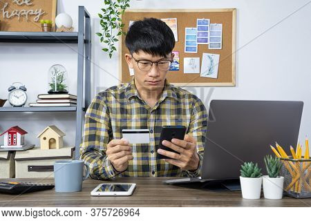 Asian Man Holding Credit Card And Typing Information On Internet With Laptop At Home, Online Shoppin