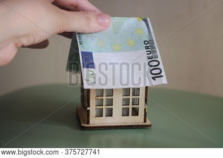Hand Puts Euro Bill Like Roof On Toy House. Buying Property Re Business Concept