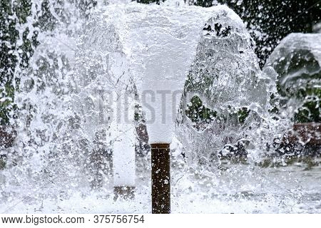 Selective Focus On Spray Of Urban Fountain And Blurred Background. A Fountain With Splashes And Drop