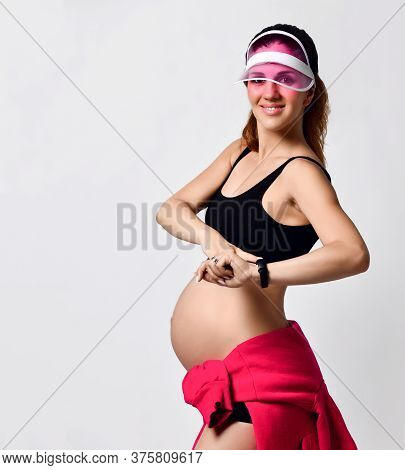 Pregnant Woman In Pink Sun Visor, Black Sport Shorts And Top. She Tied Red Hoody On Her Tummy, Smili