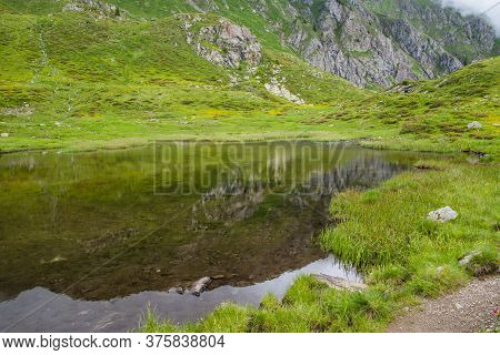 Small And Clear Alpine Lake Reflects The Mountains Around Itself In The Splendid Setting Of The Lago