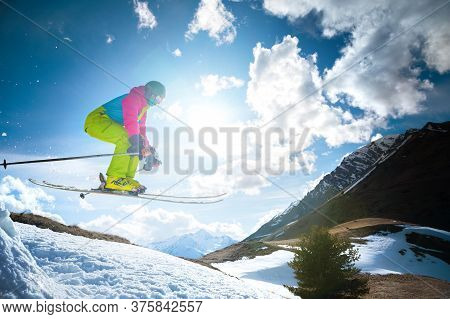 Girl Skier In Flight After Jumping From A Kicker In The Spring Against The Backdrop Of Mountains And