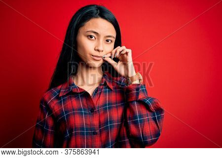 Young beautiful chinese woman wearing casual shirt over isolated red background mouth and lips shut as zip with fingers. Secret and silent, taboo talking