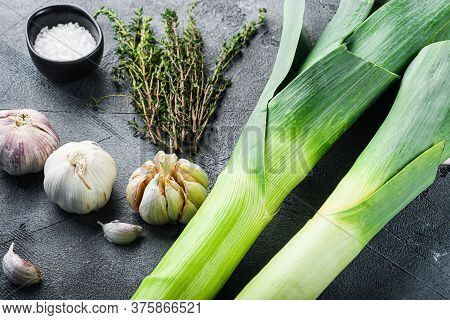 Leek Stalks With Herbs Ingredients For Coocing Braised Leeks, On Grey Textured Table Side View.