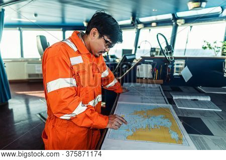Filipino Deck Officer On Bridge Of Vessel Or Ship. He Is Plotting Position On Chart