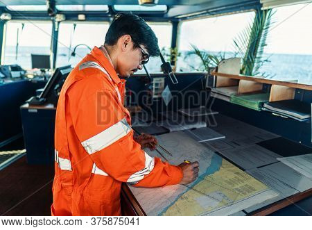 Filipino Deck Officer On Bridge Of Vessel Or Ship. He Is Plotting Position On Chart