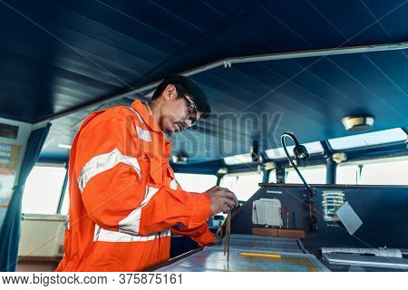 Filipino Deck Officer On Bridge Of Vessel Or Ship. He Is Plotting Position On Chart