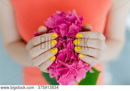 Women with manicured nails in yellow holding a flower in her hand
