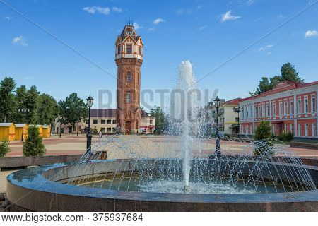 City Fountain Against The Background Of An Old Water Tower On A Sunny July Morning. Staraya Russa, R