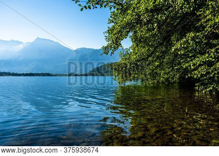 Trees Are Reflected On Lake Levico With The Mountains In The Background In Trento, Italy
