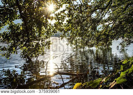Trees Are Reflected On Lake Levico With The Mountains In The Background In Trento, Italy