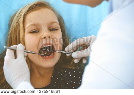 Little Baby Girl Sitting At Dental Chair With Open Mouth During Oral Check Up While Doctor. Visiting