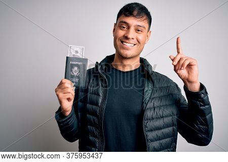 Young hispanic man holding passport document with money over isolated background surprised with an idea or question pointing finger with happy face, number one