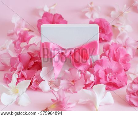 White Gift Box With A Bow Between Pink Flowers Close Up