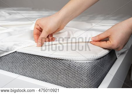 A White Satin Sheet With An Elastic Band Is Put On The Mattress Of The Bed, A Close-up Of The Hands.