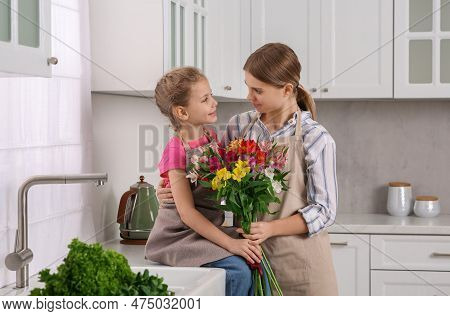 Little Daughter Congratulating Mom With Bouquet Of Flowers In Kitchen. Happy Mother's Day