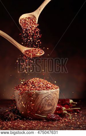 Chilli Flakes Are Poured Into A Wooden Dish. Chilli Flakes And Dried Chili Peppers On A Brown Backgr