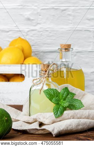 Lemon And Lime Syrups In Glass Bottle And Fruits In The Crate On The Background. Side View Of Fresh 
