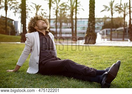 Relaxed African American Middle Aged Businessman Resting And Sitting On Grass In Park, Feeling Free,