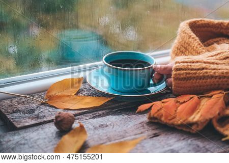Girl's Hand Holds A Cup Of Coffee On A Wooden Autumn Background. Tea And Autumn Leaves Near The Wind