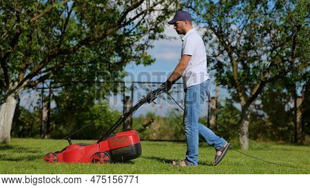 Side View Of Handsome Male Worker Working In Private Garden Mowing Lawn With Roller Machine. Man Wal