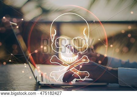 Close Up Of Male Hand Using Laptop And Cellphone At Desktop With Digital Red Skull On Blurry Backgro