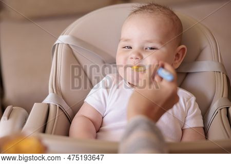 Mother Feeding Porridge To Her Happy Cheerful Baby Boy Using Spoon, Cheerful And Happy Baby Sitting 